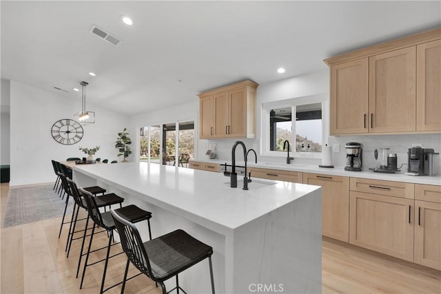 kitchen featuring pendant lighting, a center island with sink, light wood-type flooring, a kitchen breakfast bar, and light brown cabinetry