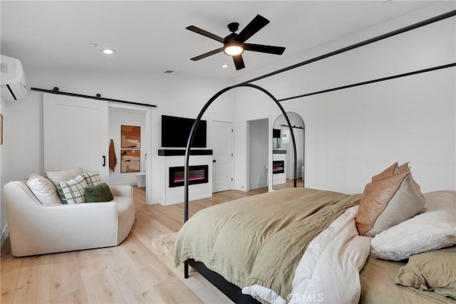 bedroom featuring ceiling fan, a barn door, lofted ceiling, light hardwood / wood-style floors, and a wall mounted air conditioner