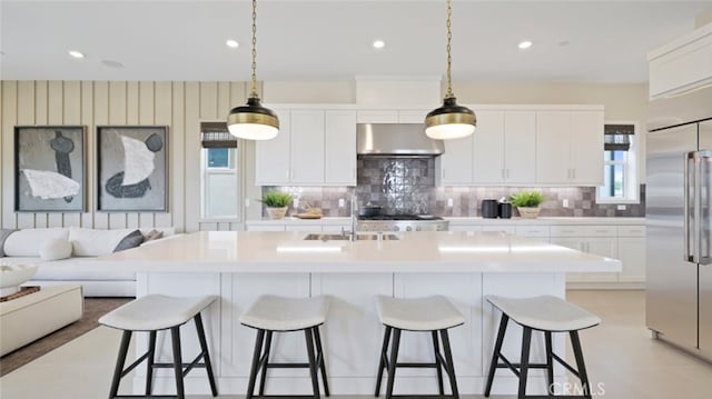 kitchen featuring stainless steel appliances, decorative backsplash, a center island with sink, white cabinets, and exhaust hood