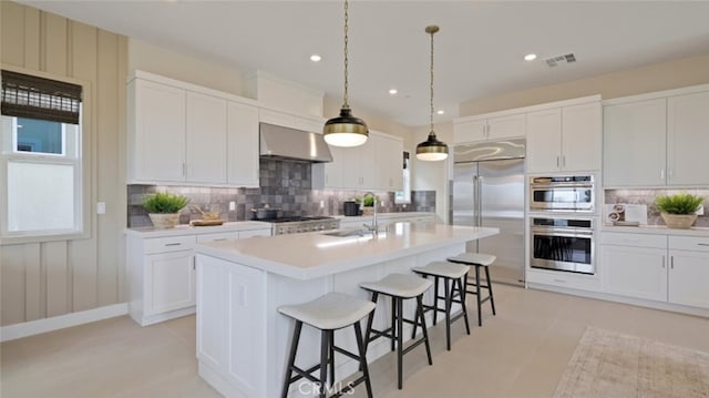 kitchen with sink, wall chimney exhaust hood, backsplash, a kitchen island with sink, and appliances with stainless steel finishes