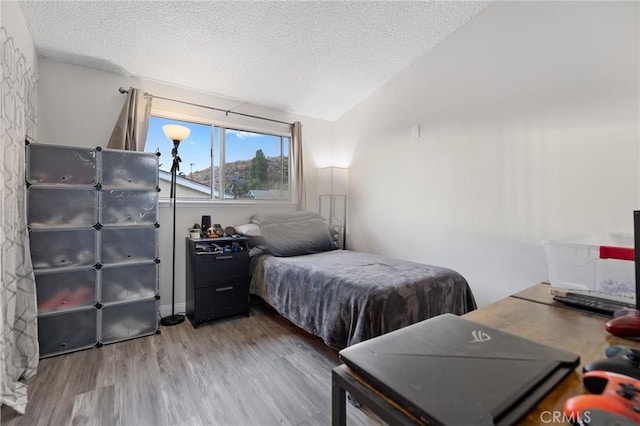 bedroom with hardwood / wood-style flooring, a textured ceiling, and vaulted ceiling