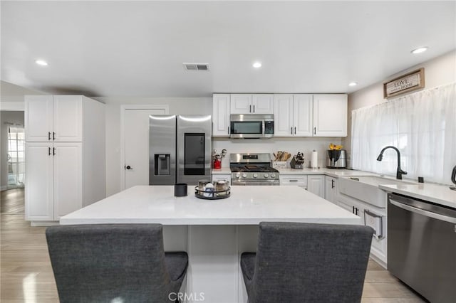 kitchen featuring appliances with stainless steel finishes, sink, white cabinets, light hardwood / wood-style floors, and a kitchen island