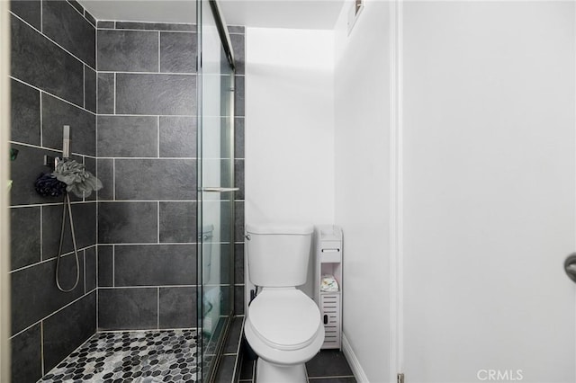 bathroom with a tile shower, tile patterned flooring, and toilet