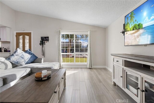 living room featuring a textured ceiling, light hardwood / wood-style floors, and lofted ceiling