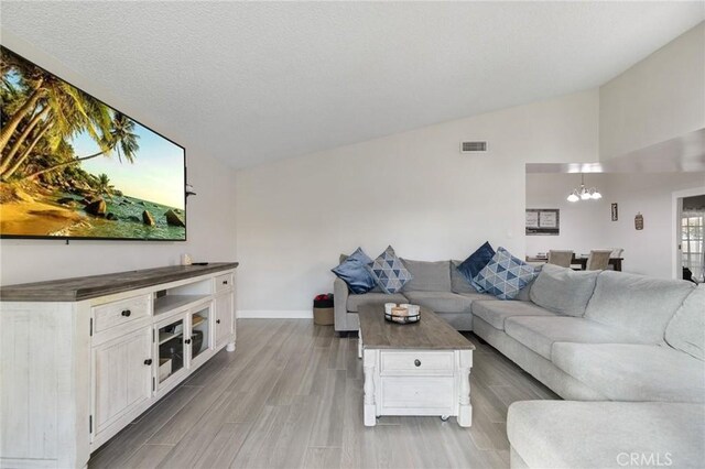 living room with hardwood / wood-style flooring, a notable chandelier, lofted ceiling, and a textured ceiling