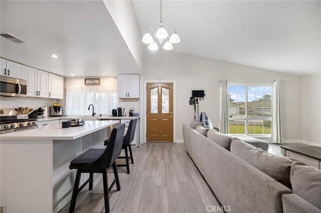 kitchen with white cabinets, a kitchen breakfast bar, light wood-type flooring, appliances with stainless steel finishes, and decorative light fixtures