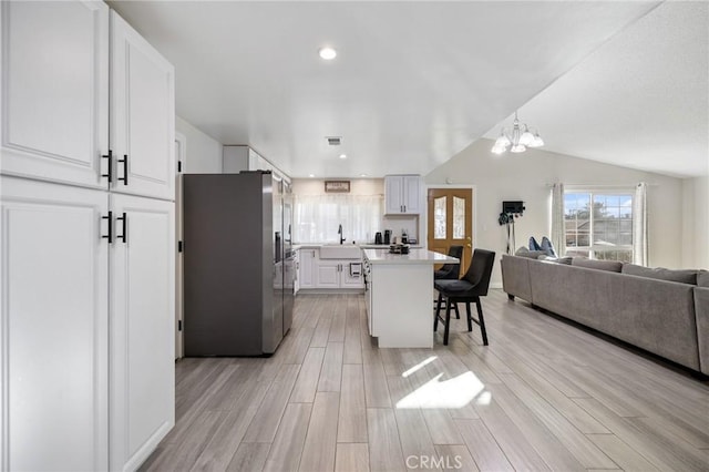 kitchen with stainless steel fridge, a kitchen breakfast bar, vaulted ceiling, white cabinets, and a kitchen island