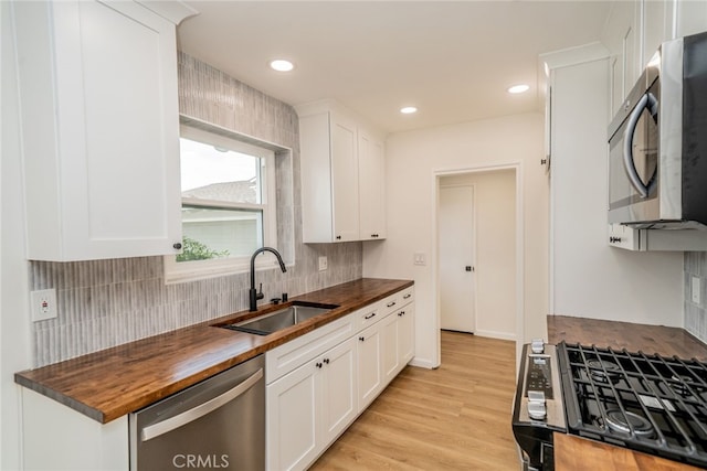 kitchen with appliances with stainless steel finishes, butcher block countertops, white cabinetry, and sink