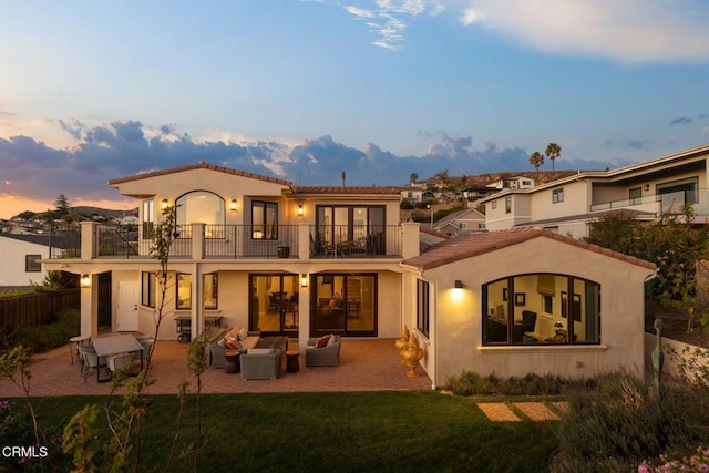 back house at dusk with an outdoor living space, a patio area, a balcony, and a yard