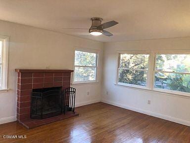 unfurnished living room with dark hardwood / wood-style flooring, ceiling fan, and a tiled fireplace