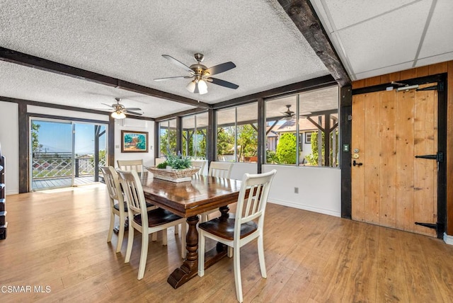 dining space featuring beamed ceiling, light hardwood / wood-style flooring, ceiling fan, and wood walls