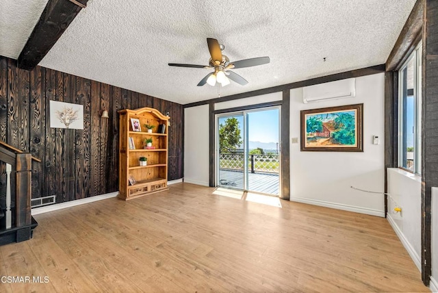 unfurnished living room featuring an AC wall unit, wooden walls, beam ceiling, and light wood-type flooring