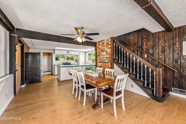 dining space featuring ceiling fan, light wood-type flooring, a textured ceiling, and wooden walls