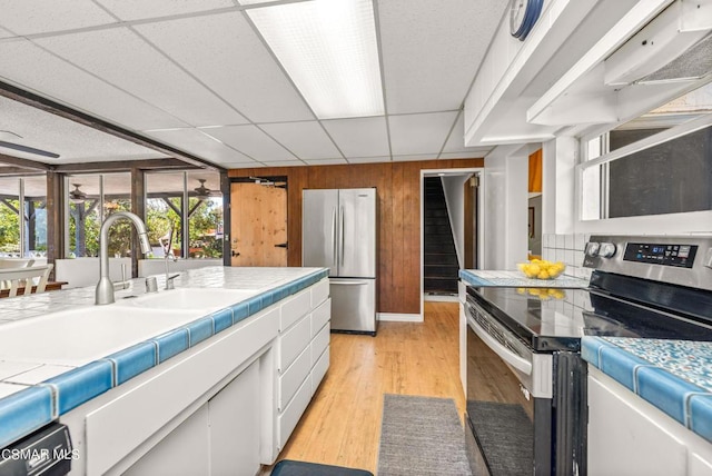 kitchen featuring stainless steel appliances, wooden walls, tile countertops, light hardwood / wood-style flooring, and white cabinets