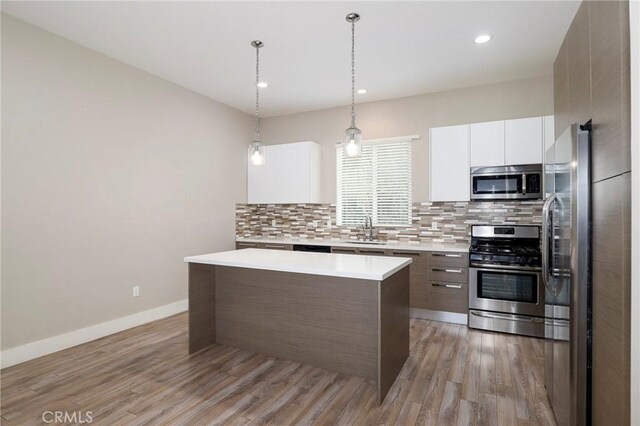 kitchen with appliances with stainless steel finishes, decorative light fixtures, white cabinets, a center island, and light hardwood / wood-style floors