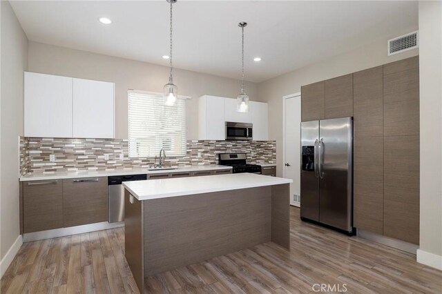 kitchen featuring decorative light fixtures, stainless steel appliances, white cabinetry, and light hardwood / wood-style flooring