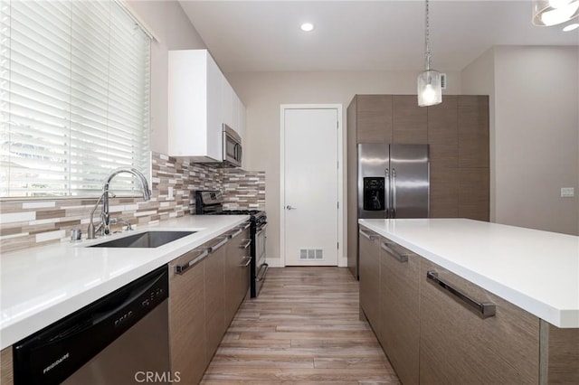 kitchen with light wood-type flooring, backsplash, stainless steel appliances, sink, and decorative light fixtures