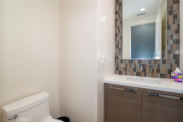 bathroom with decorative backsplash, toilet, and vanity