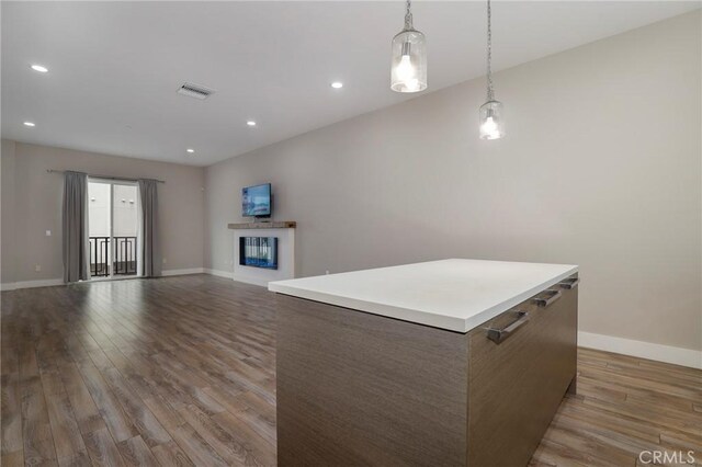 kitchen with decorative light fixtures, a center island, a multi sided fireplace, and light wood-type flooring