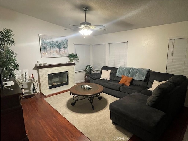 living room featuring ceiling fan, dark hardwood / wood-style floors, a textured ceiling, and a brick fireplace