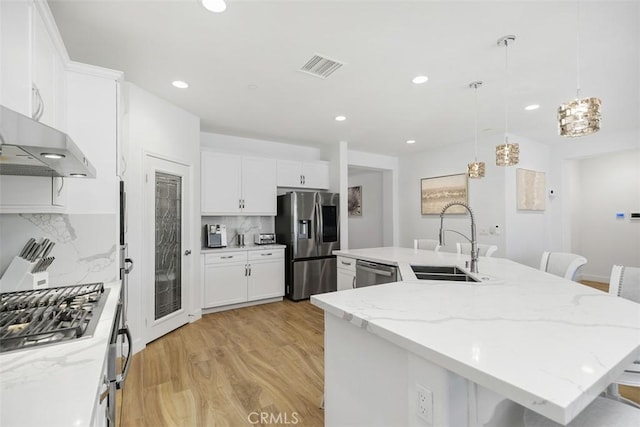 kitchen with sink, a breakfast bar area, appliances with stainless steel finishes, an island with sink, and decorative backsplash