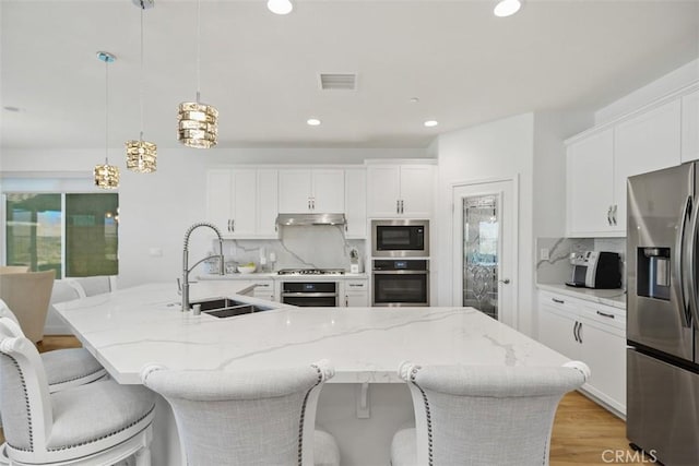 kitchen with tasteful backsplash, hanging light fixtures, an island with sink, and appliances with stainless steel finishes