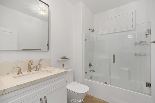 full bathroom featuring hardwood / wood-style flooring, bath / shower combo with glass door, vanity, and toilet