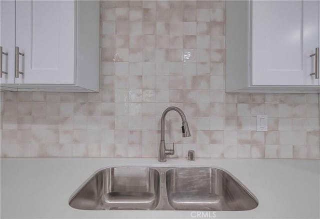 interior details with decorative backsplash, white cabinetry, and sink