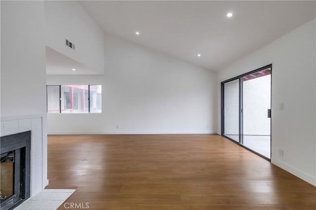 unfurnished living room with a tile fireplace, light wood-type flooring, high vaulted ceiling, and a wealth of natural light