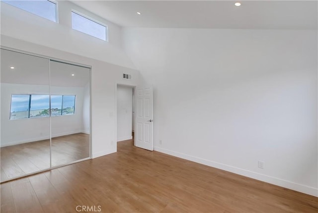 unfurnished bedroom with a closet, high vaulted ceiling, and hardwood / wood-style flooring