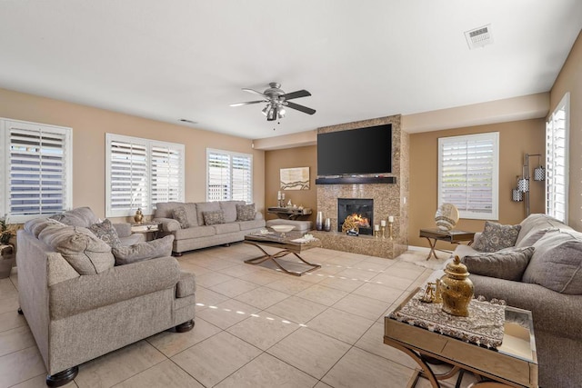 living room with ceiling fan, a large fireplace, light tile patterned floors, and a healthy amount of sunlight