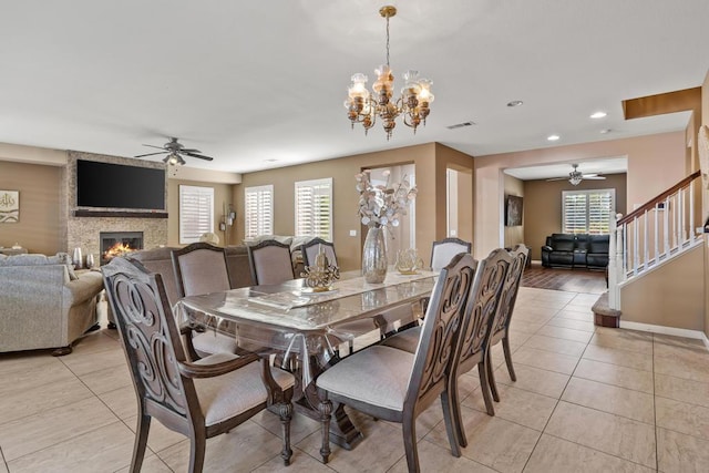 tiled dining room featuring ceiling fan with notable chandelier and a large fireplace