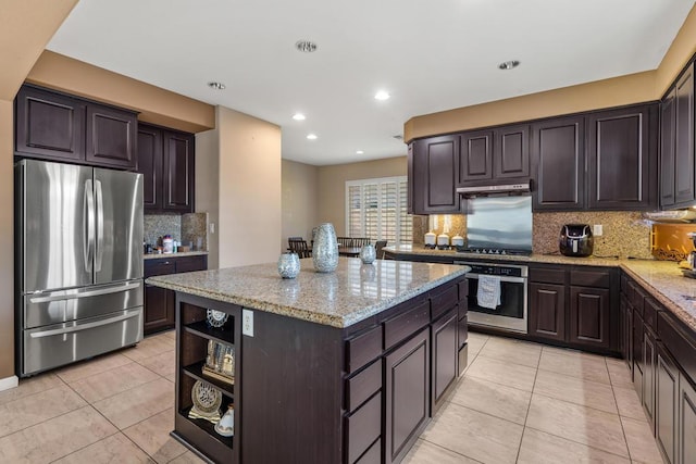 kitchen with appliances with stainless steel finishes, dark brown cabinetry, a kitchen island, and light stone counters