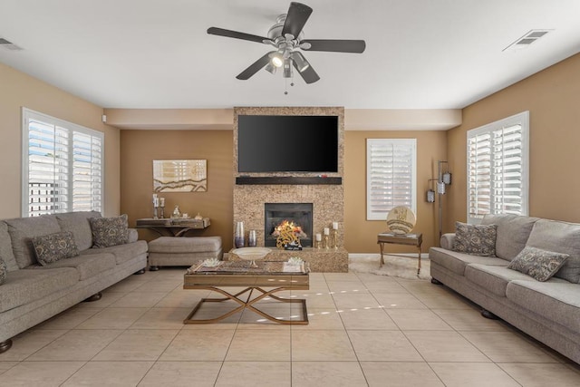 living room with ceiling fan, a large fireplace, and light tile patterned floors