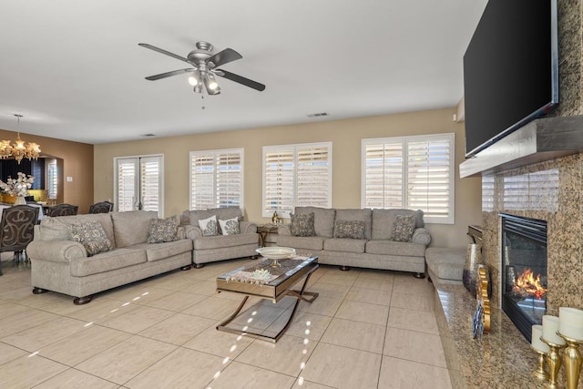 tiled living room featuring a fireplace and ceiling fan with notable chandelier