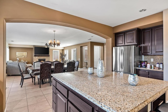 kitchen with light stone countertops, stainless steel fridge, dark brown cabinets, an inviting chandelier, and a center island