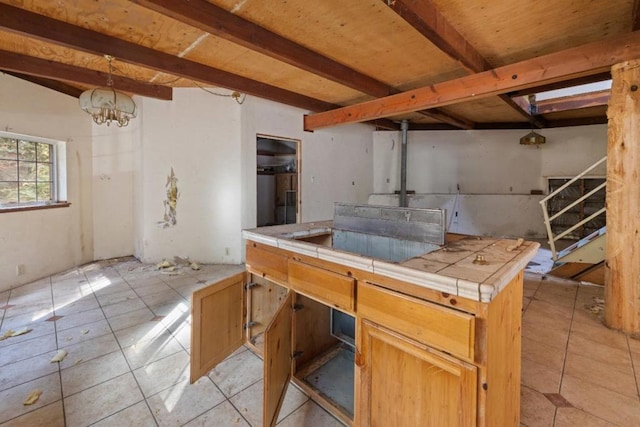 kitchen featuring pendant lighting, tile counters, light tile patterned flooring, and beamed ceiling