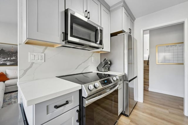 kitchen featuring appliances with stainless steel finishes, light hardwood / wood-style flooring, backsplash, and light stone counters