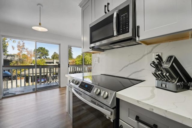 kitchen featuring light stone countertops, pendant lighting, stainless steel appliances, gray cabinets, and backsplash