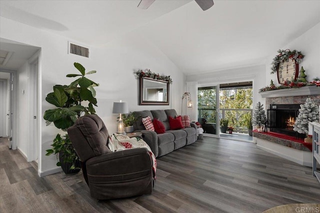 living room featuring dark wood-type flooring, lofted ceiling, and a stone fireplace