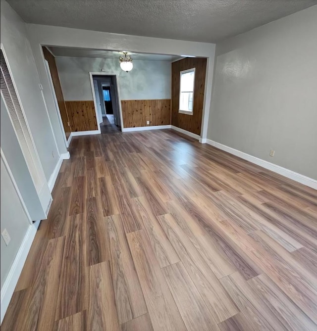 unfurnished living room featuring hardwood / wood-style flooring, a textured ceiling, and wood walls