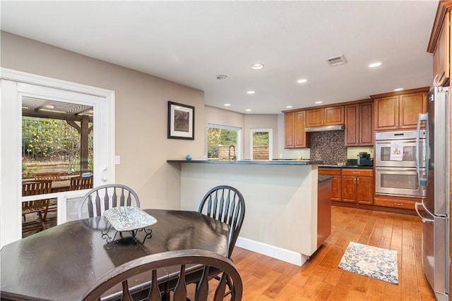 kitchen featuring sink, light hardwood / wood-style flooring, decorative backsplash, appliances with stainless steel finishes, and kitchen peninsula