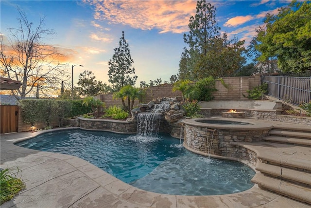 pool at dusk featuring an in ground hot tub and pool water feature