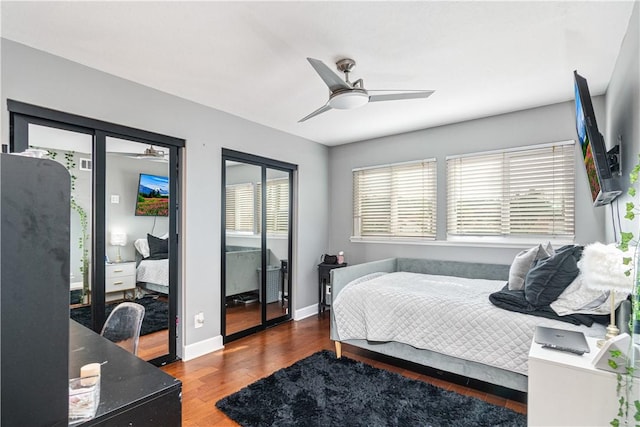 bedroom with multiple windows, dark hardwood / wood-style flooring, two closets, and ceiling fan