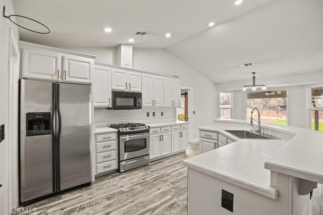 kitchen with lofted ceiling, white cabinets, appliances with stainless steel finishes, and sink