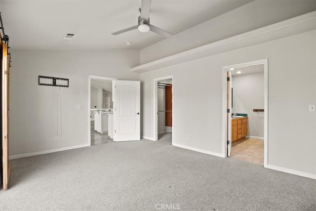 unfurnished bedroom featuring ensuite bath, light carpet, vaulted ceiling, ceiling fan, and a barn door