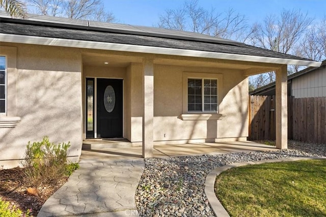 property entrance with solar panels, fence, and stucco siding