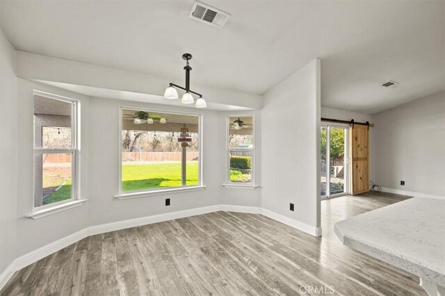 unfurnished dining area with ceiling fan, a barn door, and hardwood / wood-style flooring