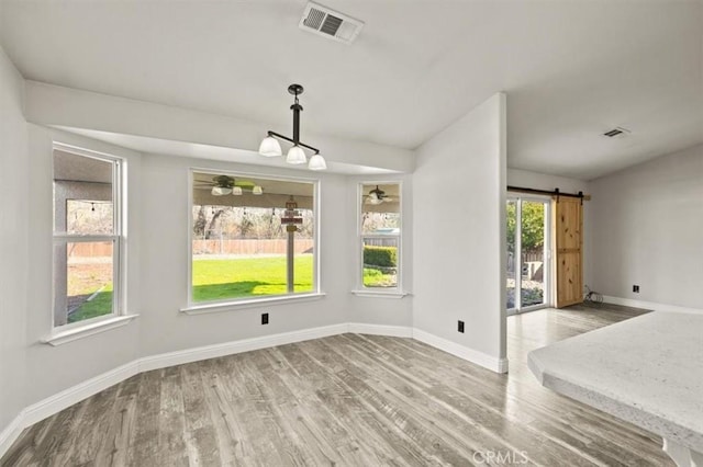 unfurnished dining area with visible vents, wood finished floors, a barn door, baseboards, and ceiling fan