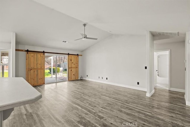 unfurnished living room with ceiling fan, a barn door, vaulted ceiling, and hardwood / wood-style flooring